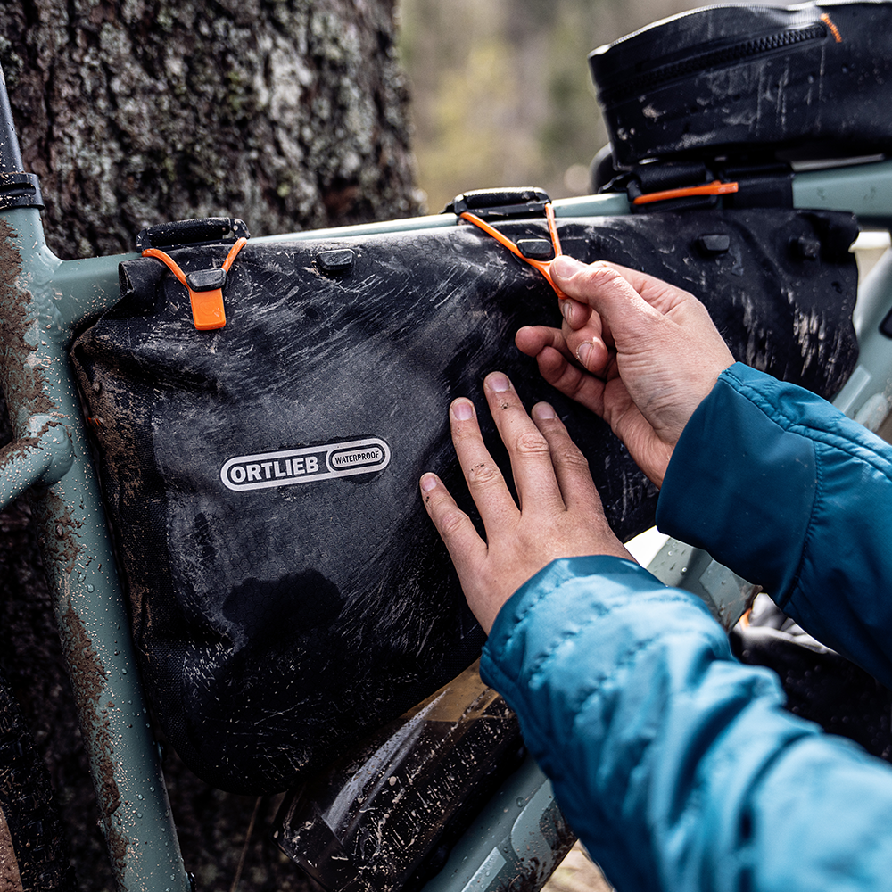 Die meisten puristischen Bikepacking-Taschen werden mit robusten Klettverschlüssen oder gummierten Spannriemen (Straps) direkt am Rahmen fixiert.